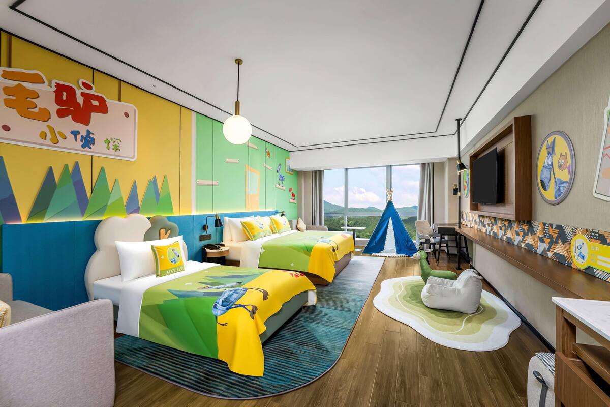 Habitación de hotel con dos camas, televisión, escritorio y un amplio ventanal con vistas.