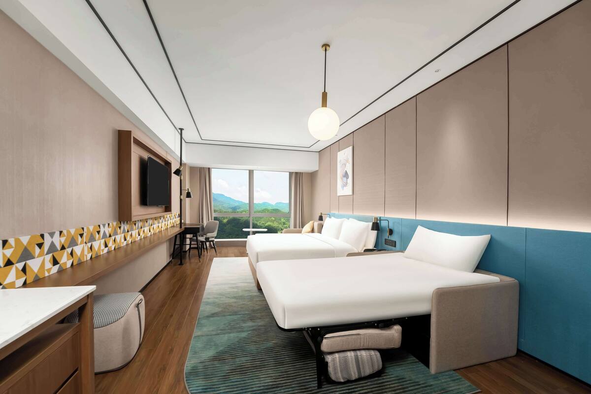 Habitación de hotel con dos camas, un escritorio, una silla, televisión y vistas a la montaña.