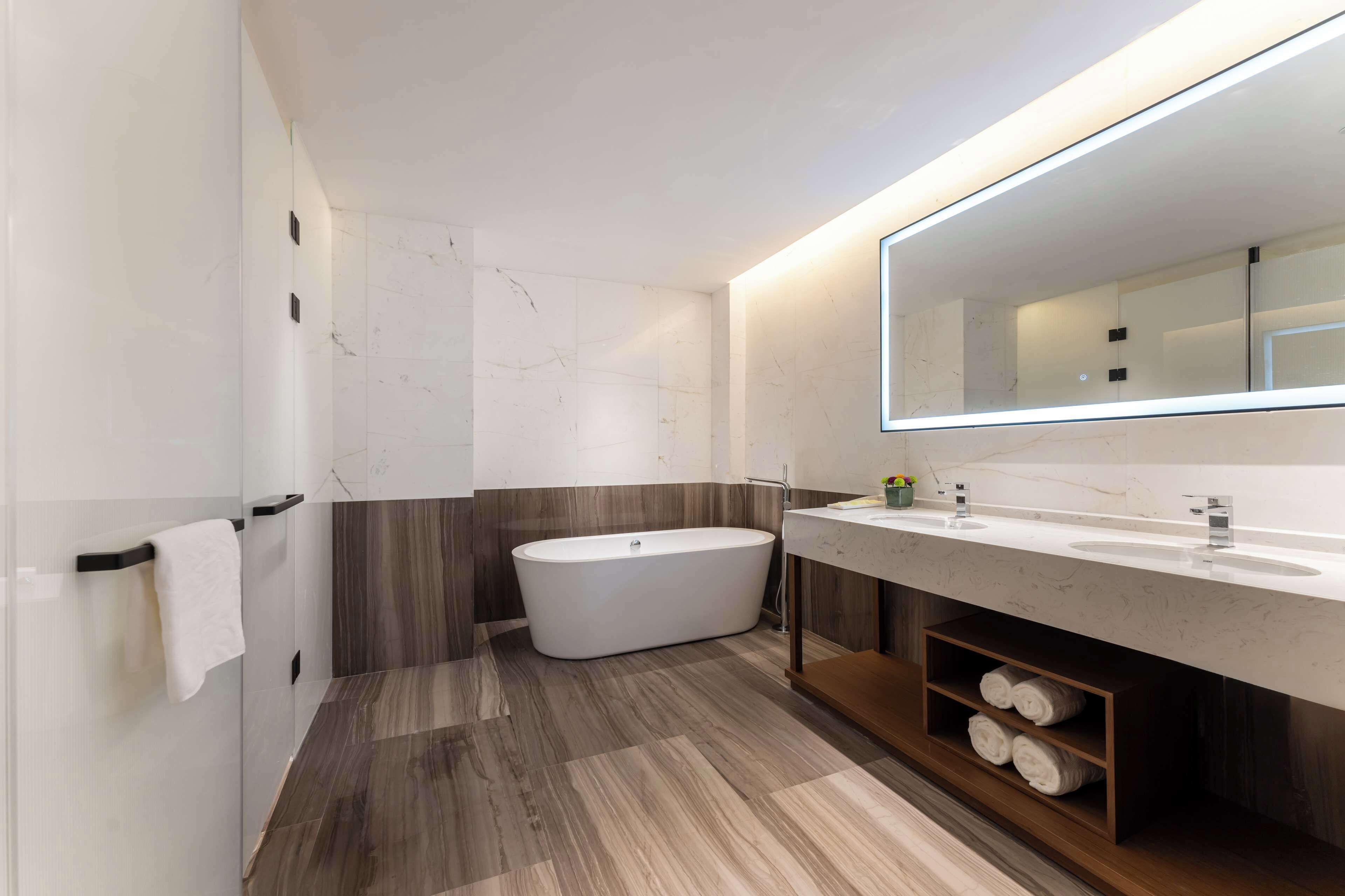 A modern bathroom with a freestanding bathtub, a large mirror, and a vanity with two sinks.
