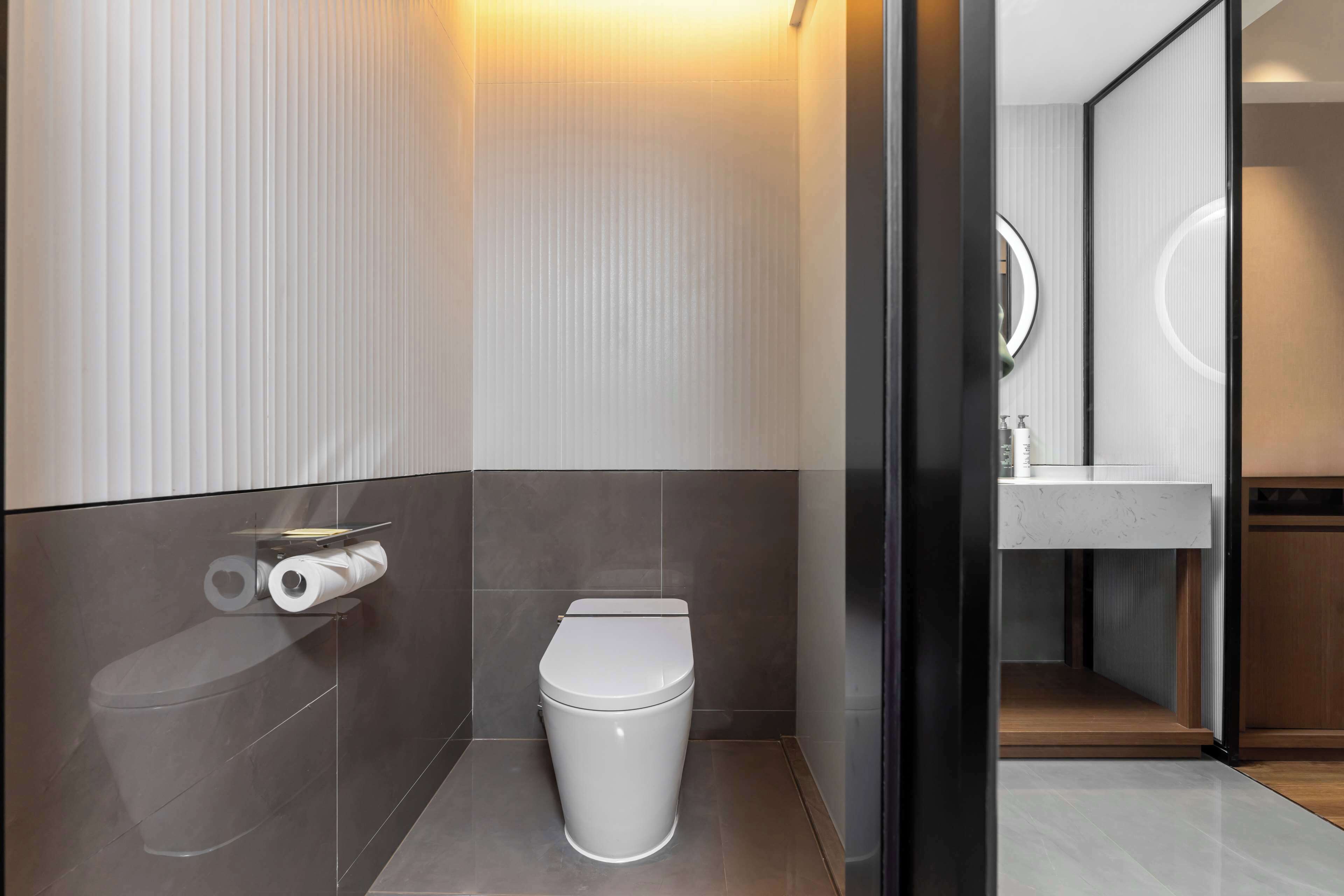 Egy modern fürőszoba, amelyben található egy WC, WC-papírtartó és egy tükör.