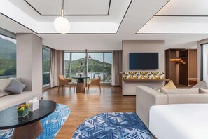 Una habitación de hotel moderna con un ventanal grande, un sofá, una mesa de comedor y un televisor en la pared.