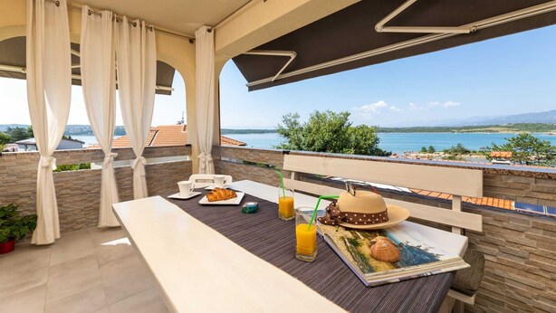 Un balcon avec une table dressée pour le petit-déjeuner, offrant une vue panoramique sur la mer et les collines.