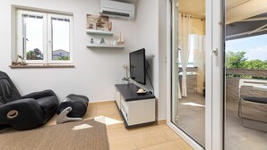 Un salon moderne comprenant un canapé, un fauteuil massant, un téléviseur à écran plat et une porte-fenêtre coulissante donnant sur une terrasse extérieure.