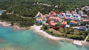 Vue aérienne d’une zone résidentielle côtière, avec des maisons, une plage et une mer bleue et limpide.