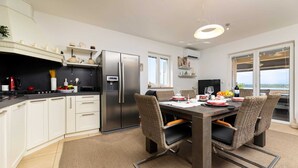 Une cuisine moderne avec des meubles blancs, un réfrigérateur en acier inoxydable et un coin repas comprenant des chaises en osier et une table en bois.