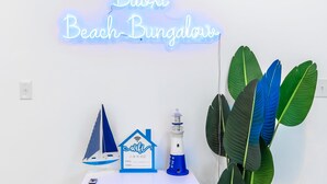 Ein leuchtendes Neon-Schild mit der Aufschrift "Biloxi Beach Bungalow", kombiniert mit einem kleinen Segelboot, einem Leuchtturm und einem haussymbolartigen Schild, das kostenloses WLAN anzeigt.