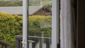 A view through a glass door of a building with a wooden roof, surrounded by greenery. - Beech (Swanage)
