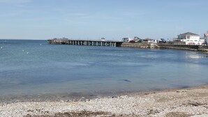 A coastal scene with a pier extending into the sea, a small building, and a rocky shoreline. - Beech (Swanage)