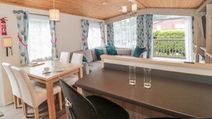 A cozy room with a wooden ceiling, a sofa with cushions, a dining table with chairs, and a large window with curtains. - Beech (Swanage)