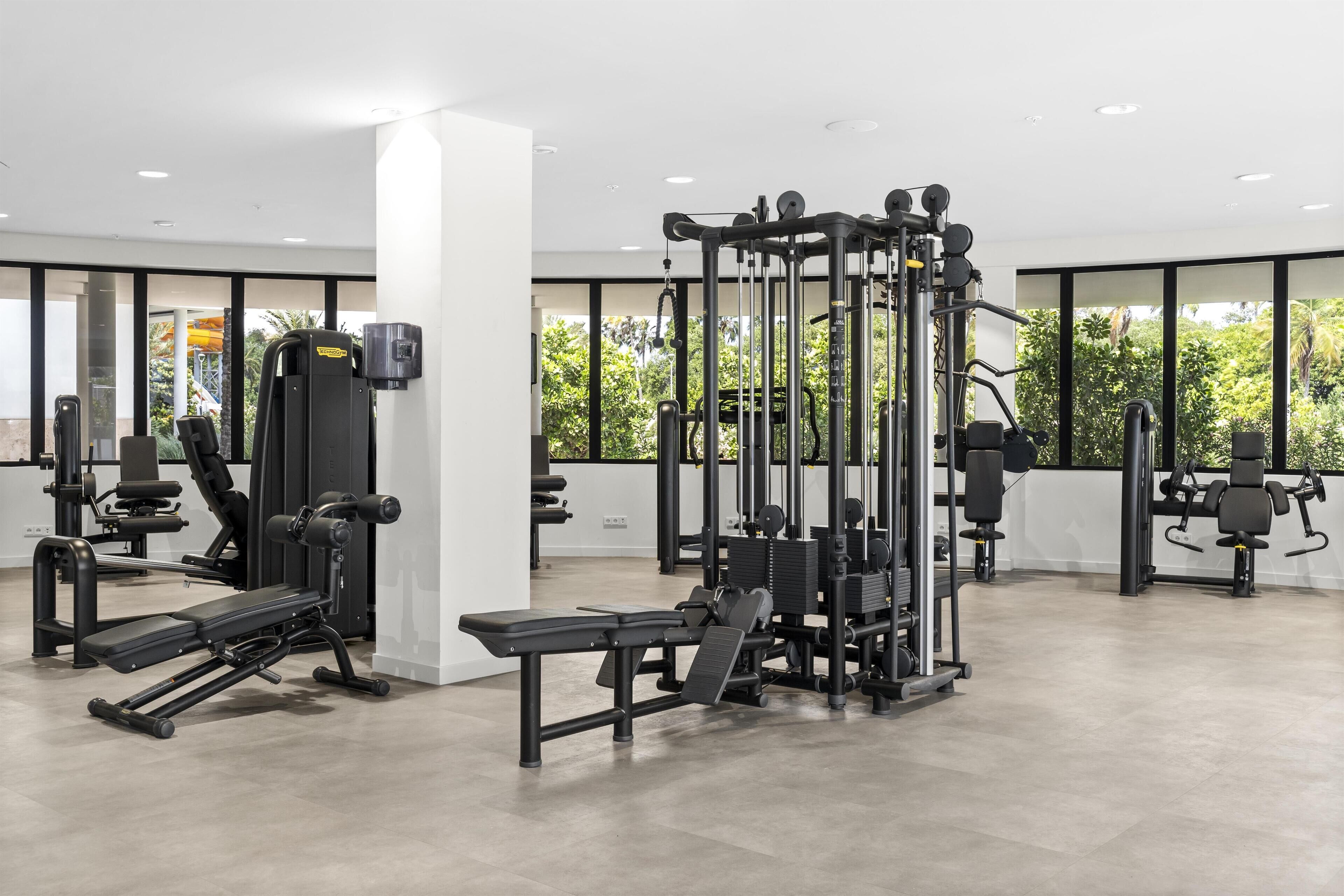 A modern gym with various exercise equipment, large windows, and a clean, spacious layout.