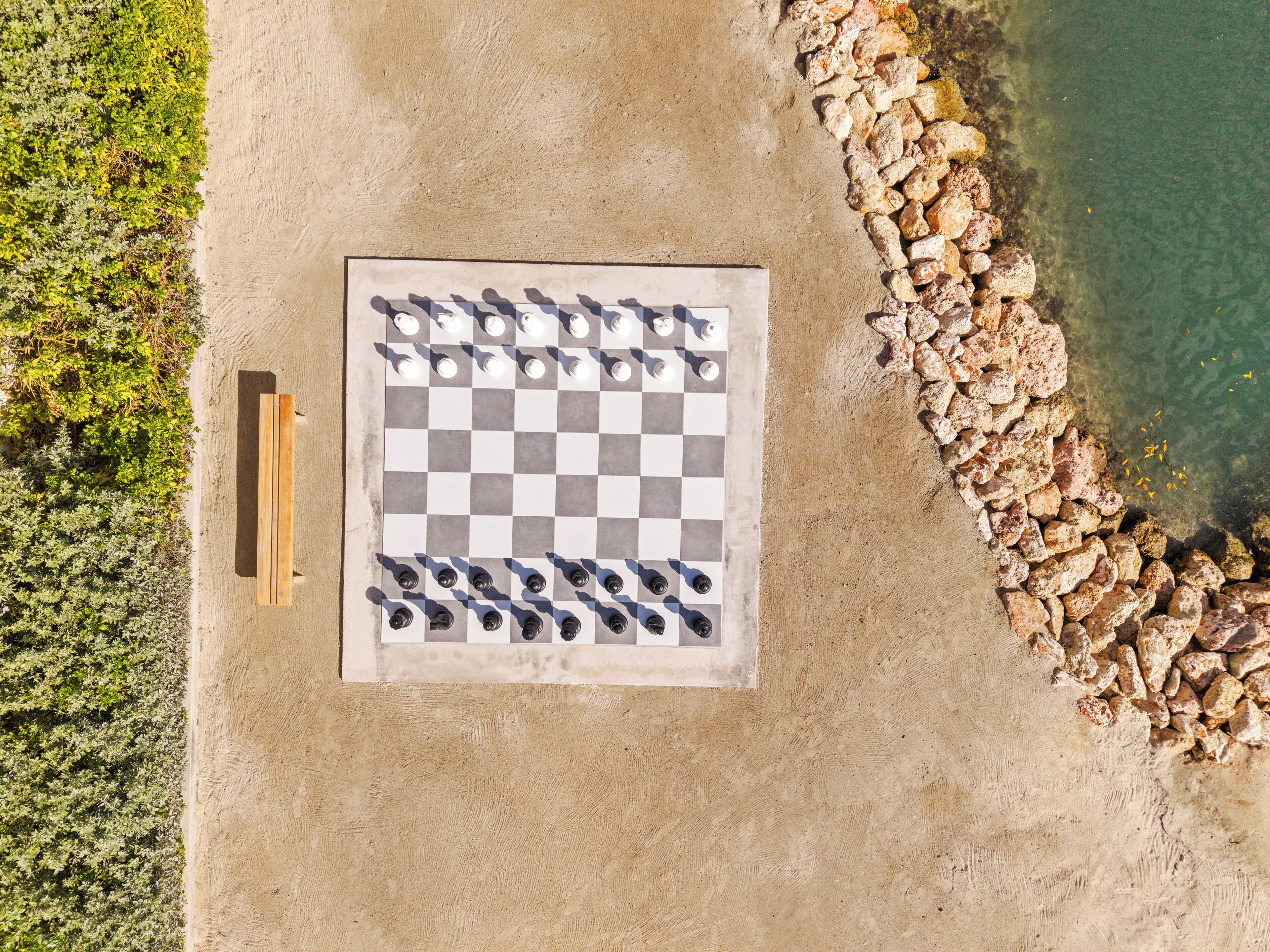 Vista aérea de una playa con un tablero de juego a cuadros y un banco de madera.