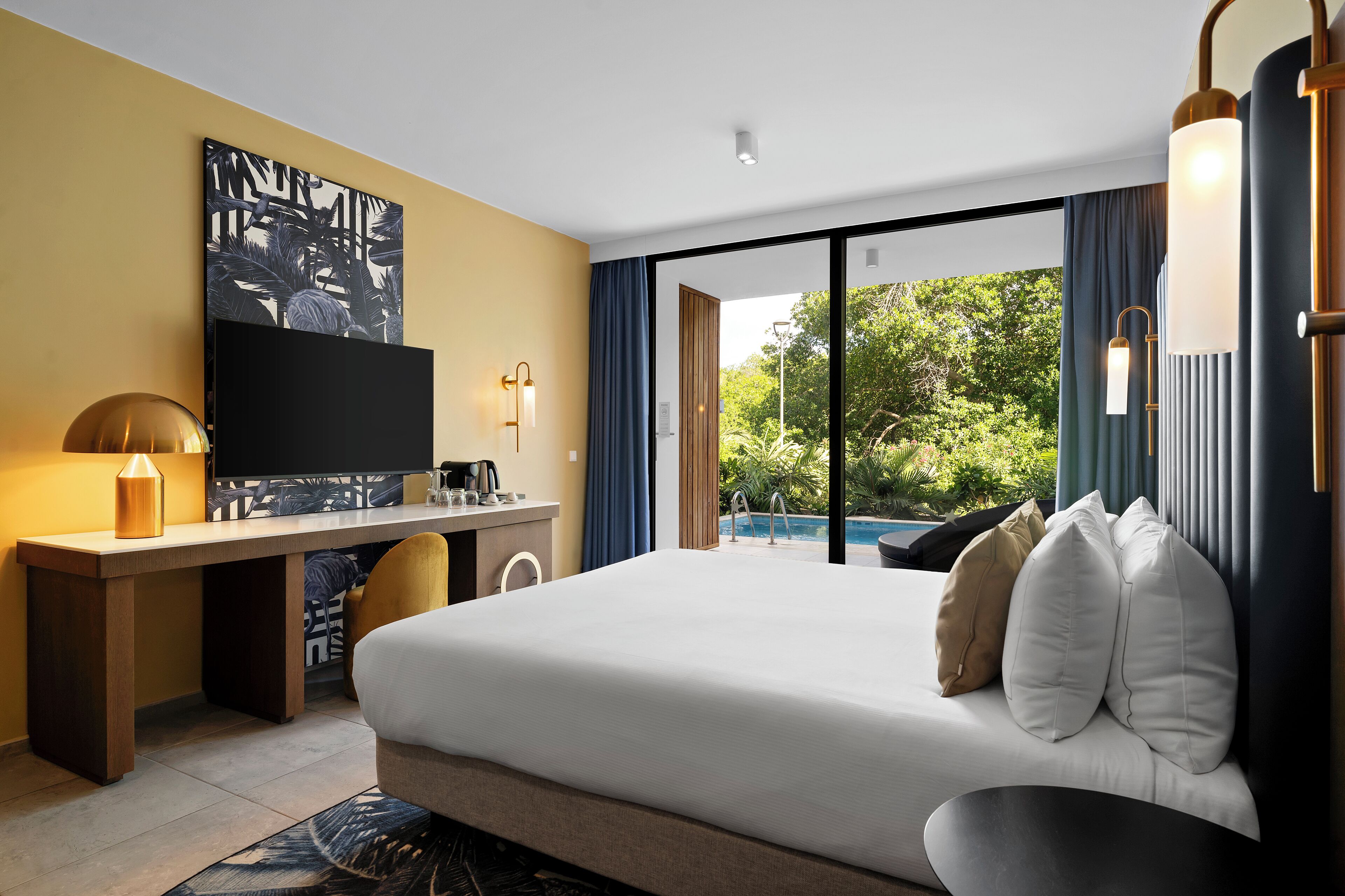 A modern hotel room with a large bed, a desk with a flat-screen TV, a coffee maker, and a view of a swimming pool.