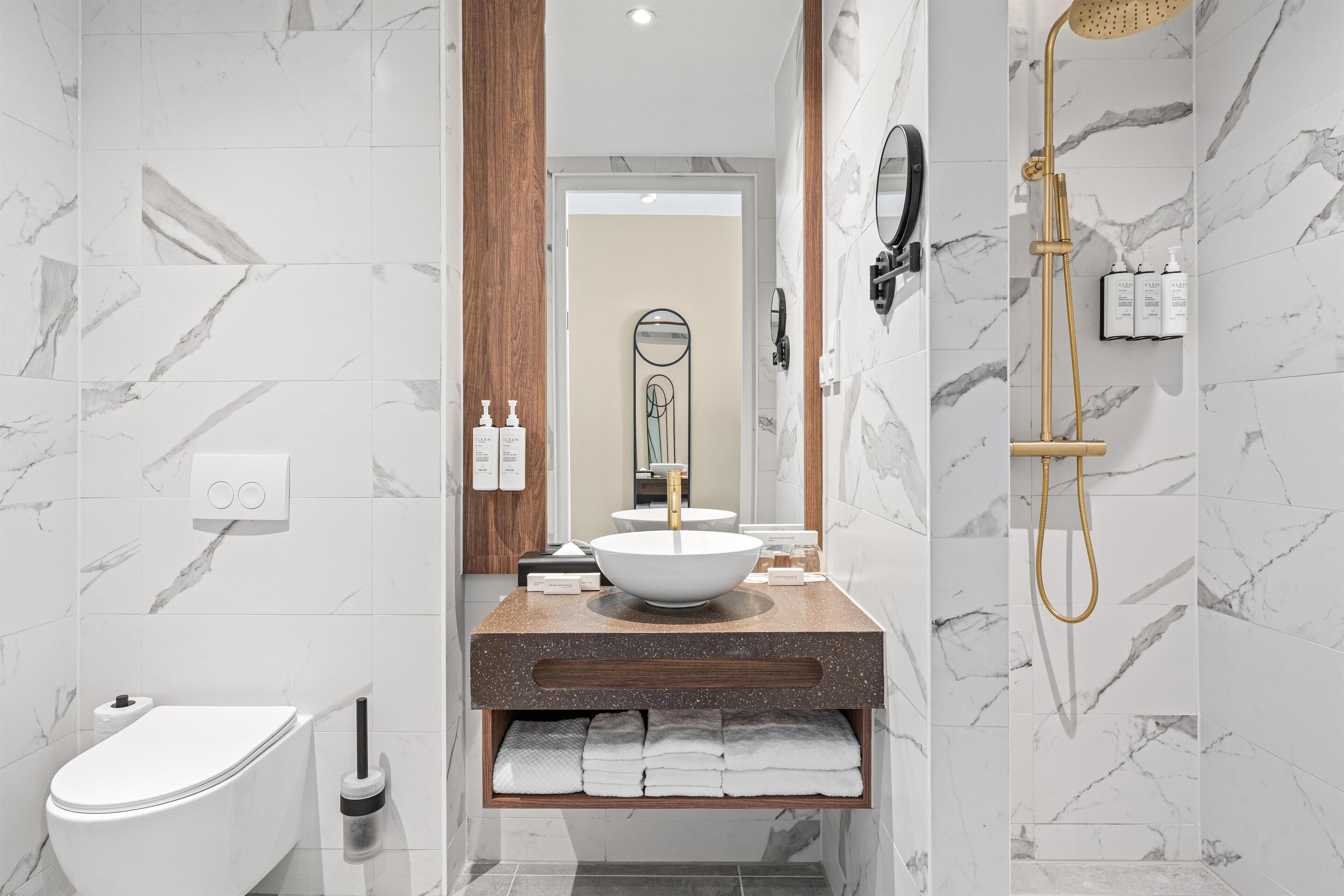 A modern bathroom with a white toilet, a large sink with a gold faucet, and a shower with a gold showerhead.