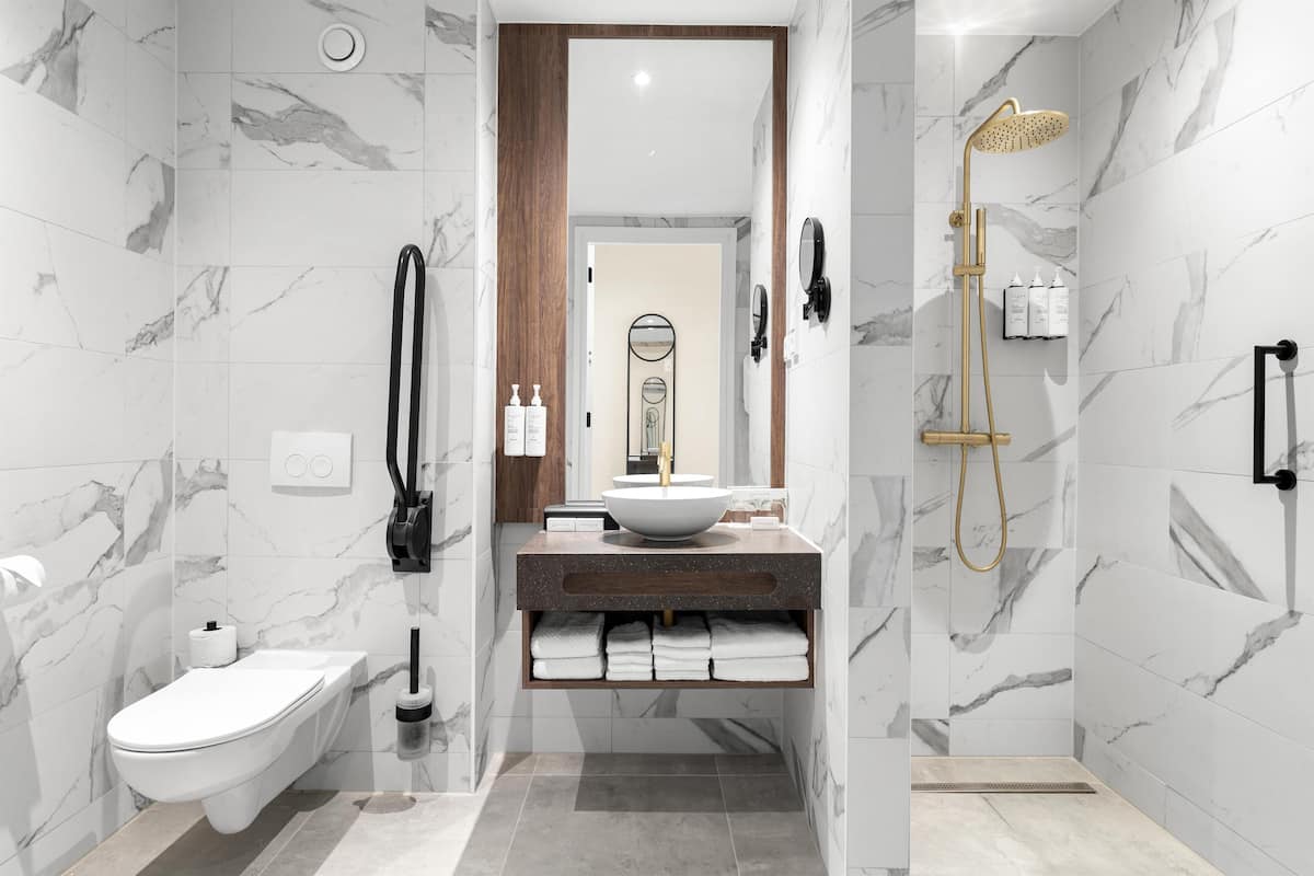 A modern bathroom with a marble wall, a wooden vanity, a toilet, and a shower with a gold showerhead.