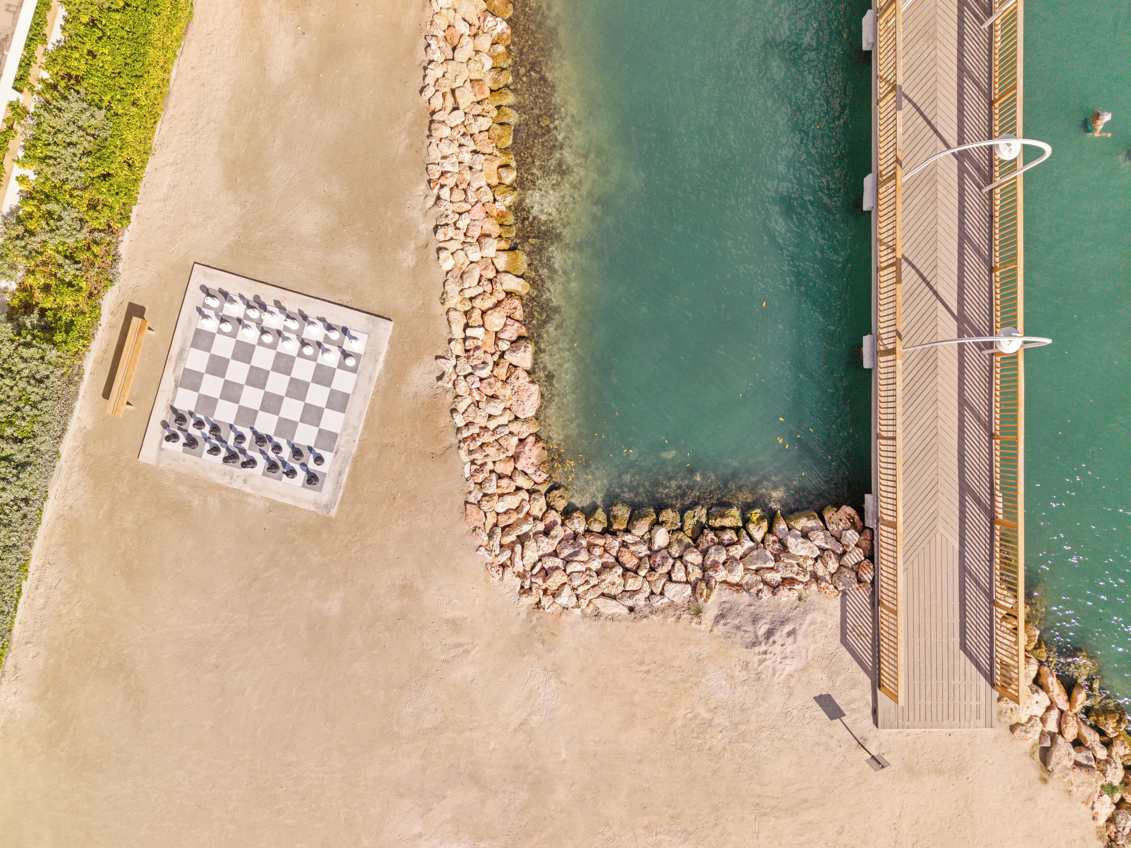 An aerial view of a beach with a checkered game board, a wooden deck, and a rocky shoreline.