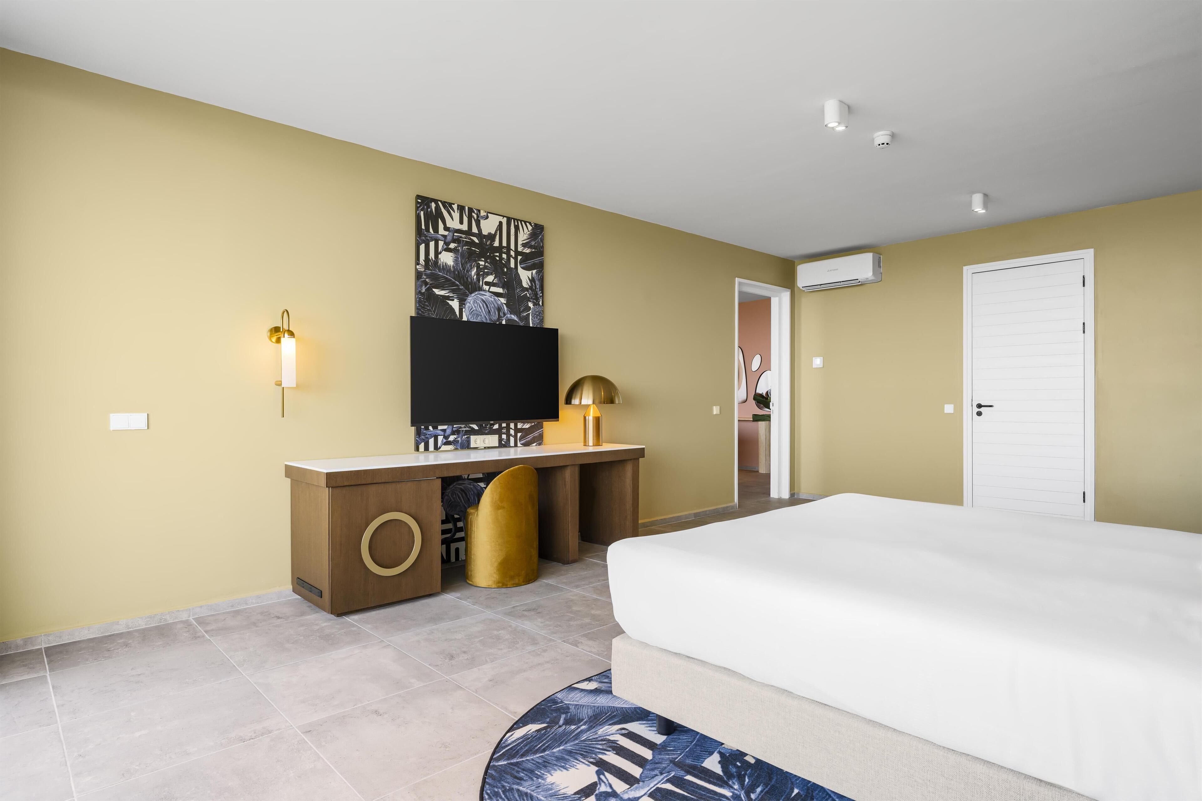 Habitación de hotel con cama, escritorio, televisor de pantalla plana, lámpara de pared y puerta.