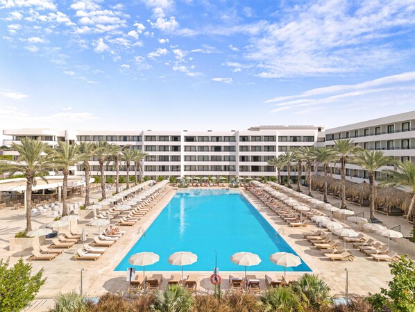 A hotel with a large pool, sun loungers, and palm trees.