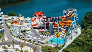 A water park with multiple slides and pools, surrounded by palm trees and outdoor seating areas.