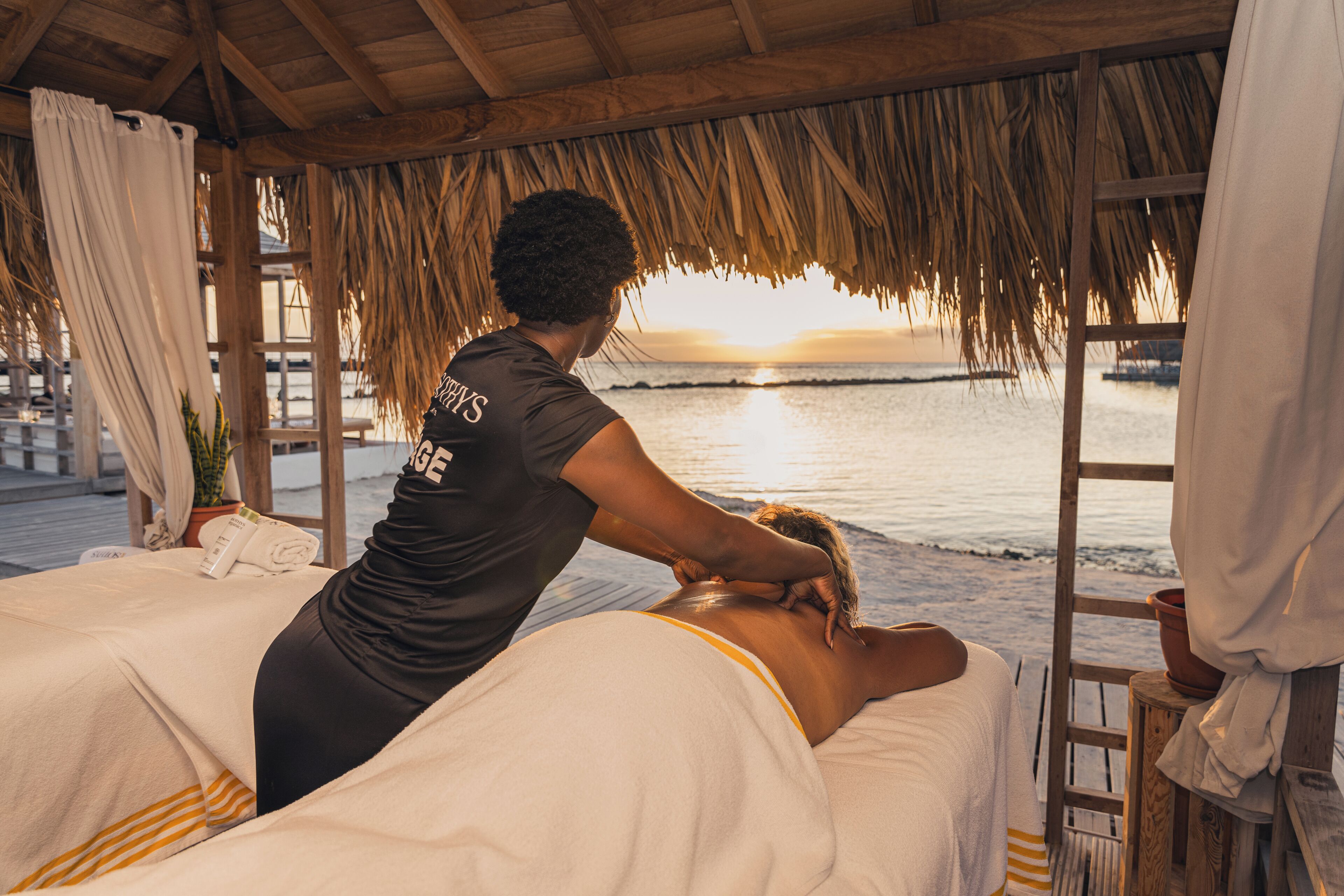 A massage therapy session in a wooden room with a view of the ocean at sunset.