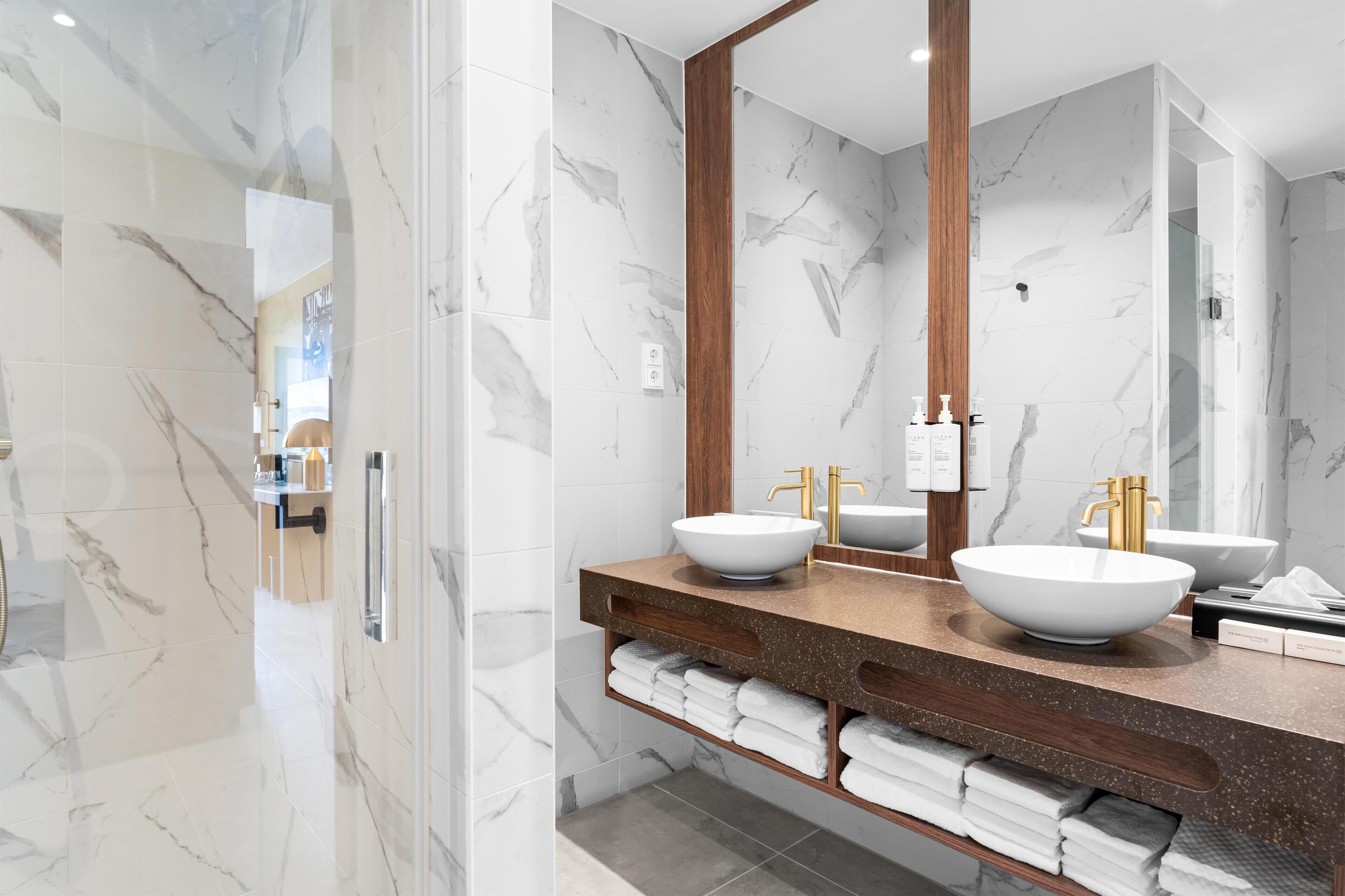 Un baño moderno con paredes de mármol, dos lavamanos con grifos dorados y un espejo grande.