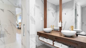 Un baño moderno con paredes de mármol, dos lavamanos con grifos dorados y un espejo grande.