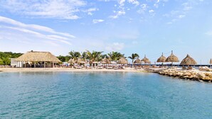 A beachside resort with thatched-roof structures, palm trees, and lounge chairs along the shoreline.