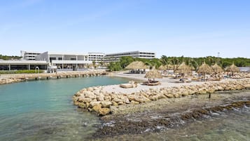 A coastal hotel with a beach area, including lounge chairs and umbrellas, and a clear view of the sea.