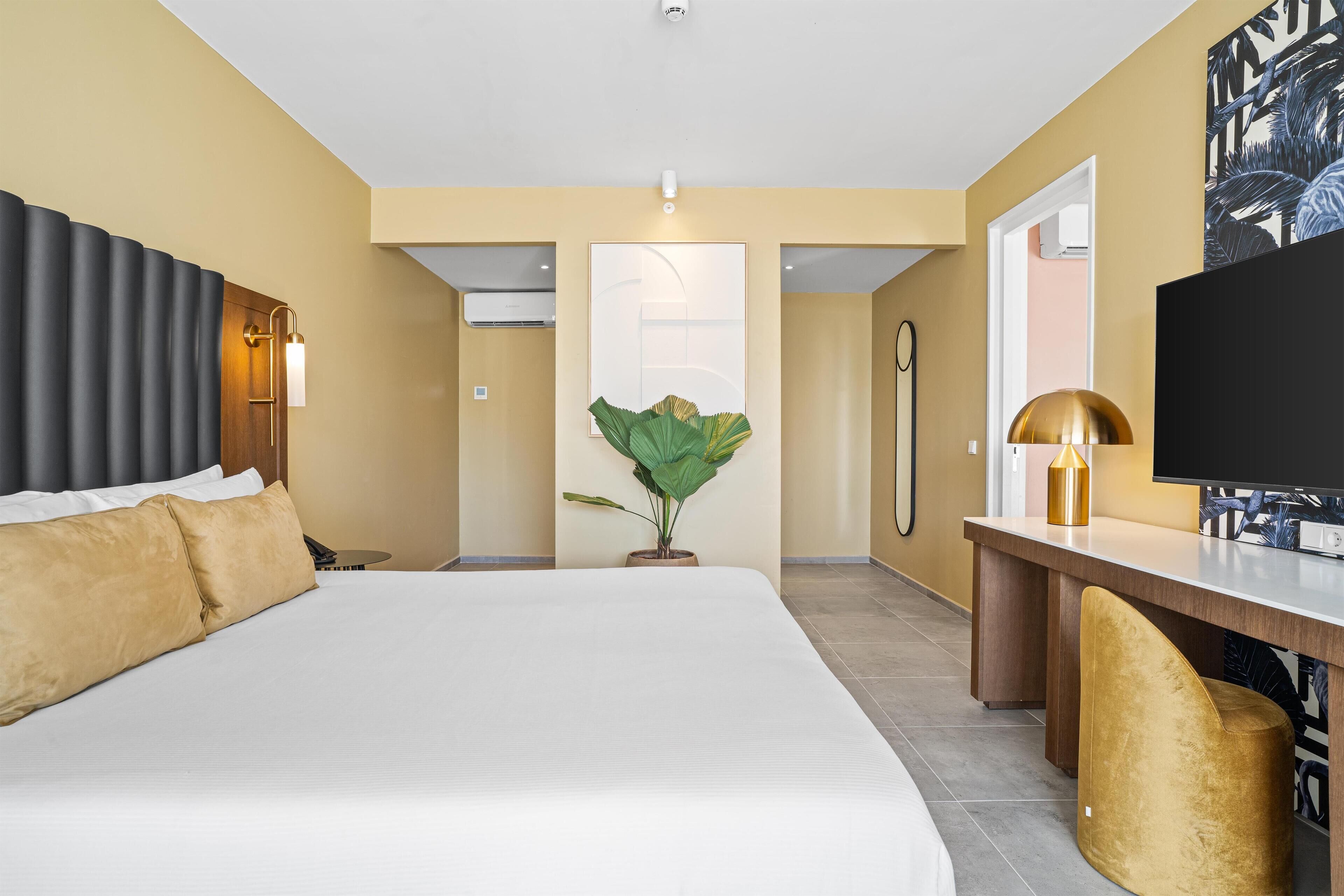 Habitación de hotel con una cama grande, un escritorio, un televisor y una planta en maceta.