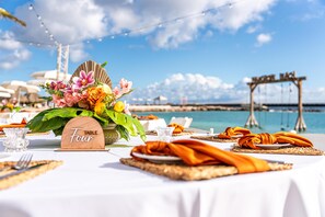 A table set with a floral centerpiece, a wooden sign indicating 'TABLE FOUR,' and a view of the sea and a bridge in the background.