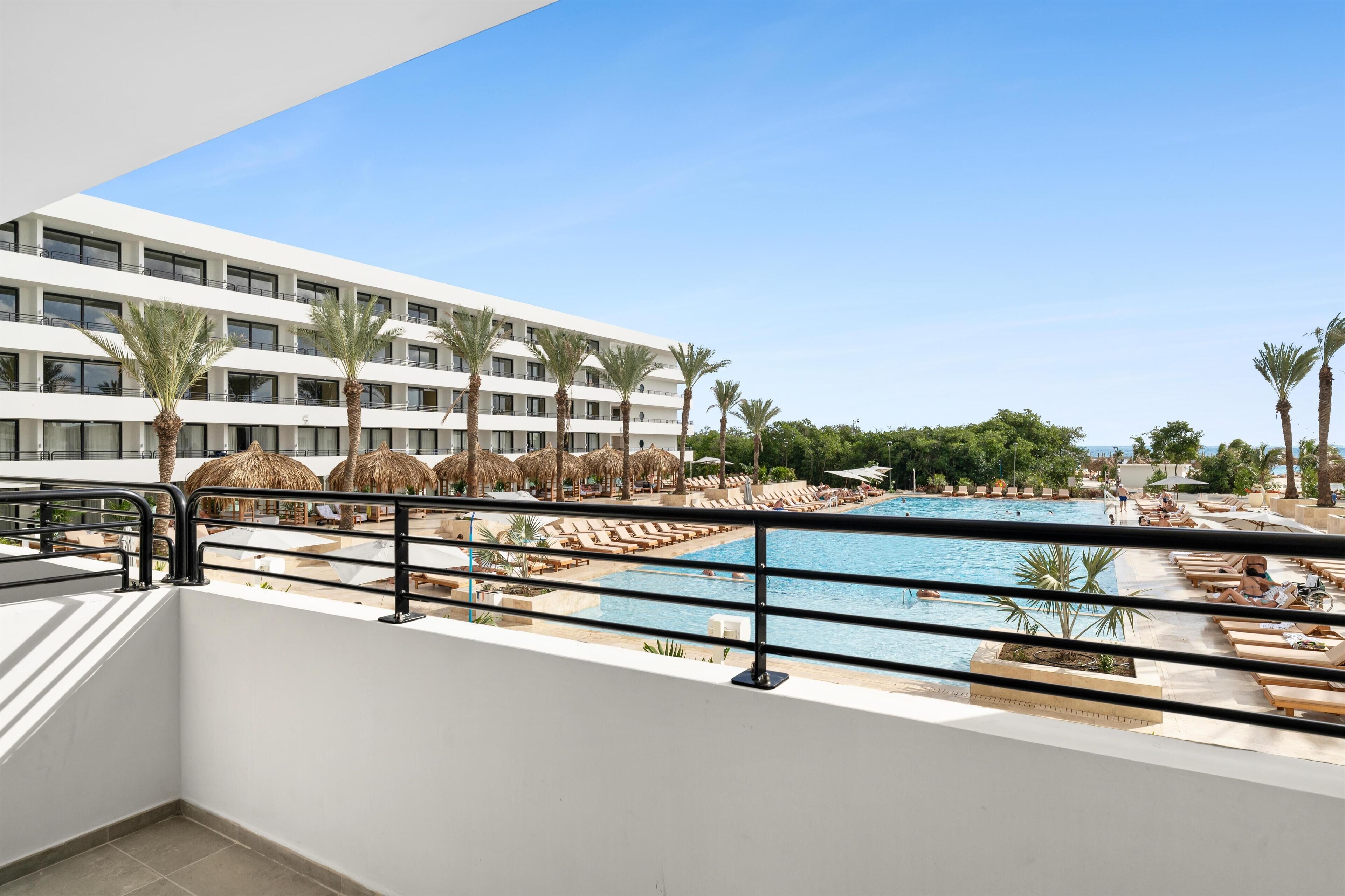 A hotel with a pool area, including sun loungers and umbrellas, and a view of the pool from a balcony.