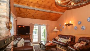 Ein gemütliches Wohnzimmer mit Ledersofas, einem Kamin, einem Fernseher und einer Holzbalkendecke.