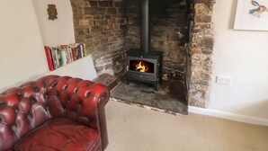 A cozy living room with a stone fireplace, a red leather sofa, and a bookshelf filled with books. - Brewers Cottage (Umberleigh)
