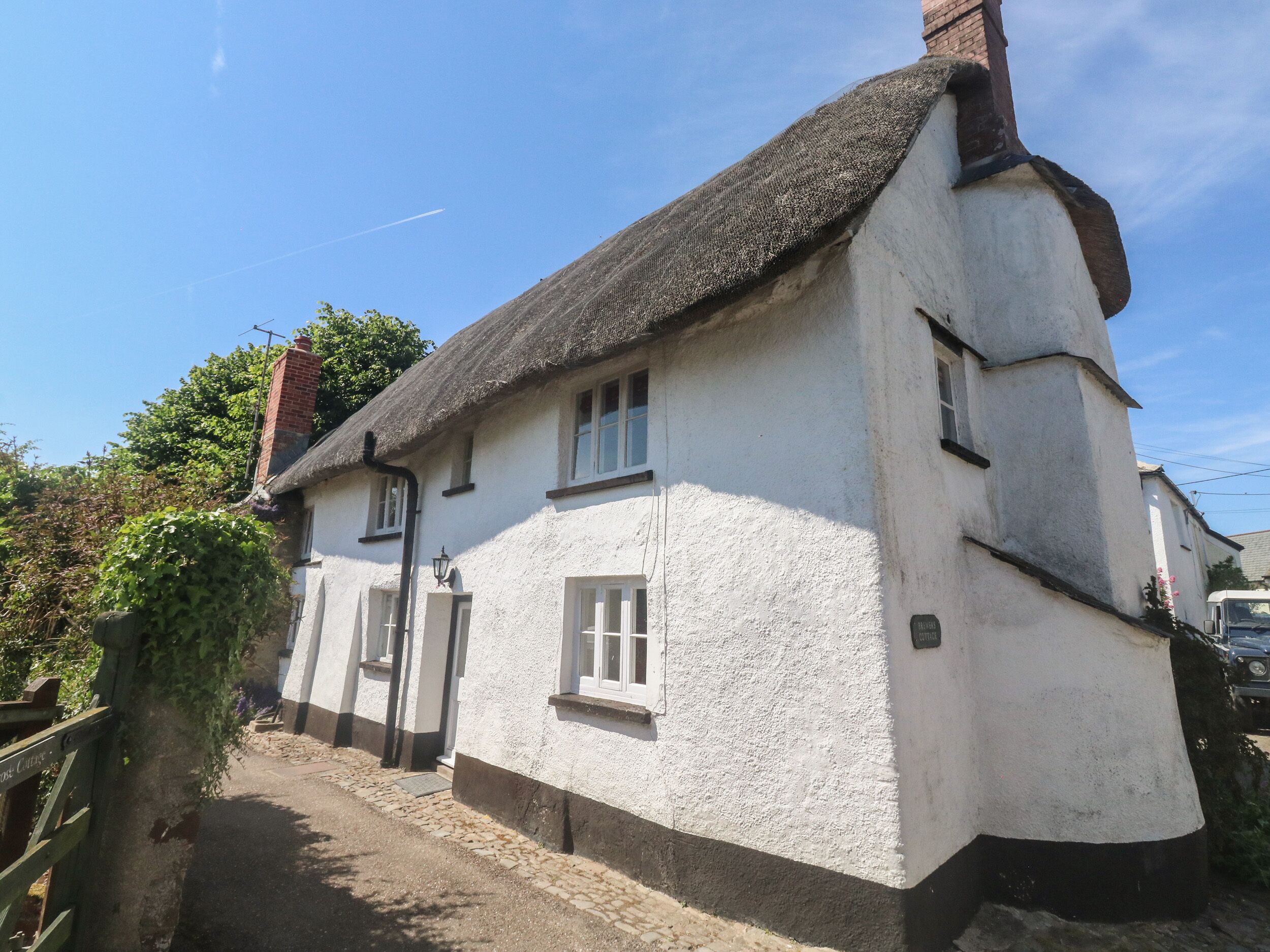 A traditional white building with a thatched roof, a visible chimney, and a small garden area.