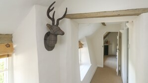 A hallway with a mounted deer head on the wall, a window with a curtain, and a wooden beam ceiling. - Brewers Cottage (Umberleigh)