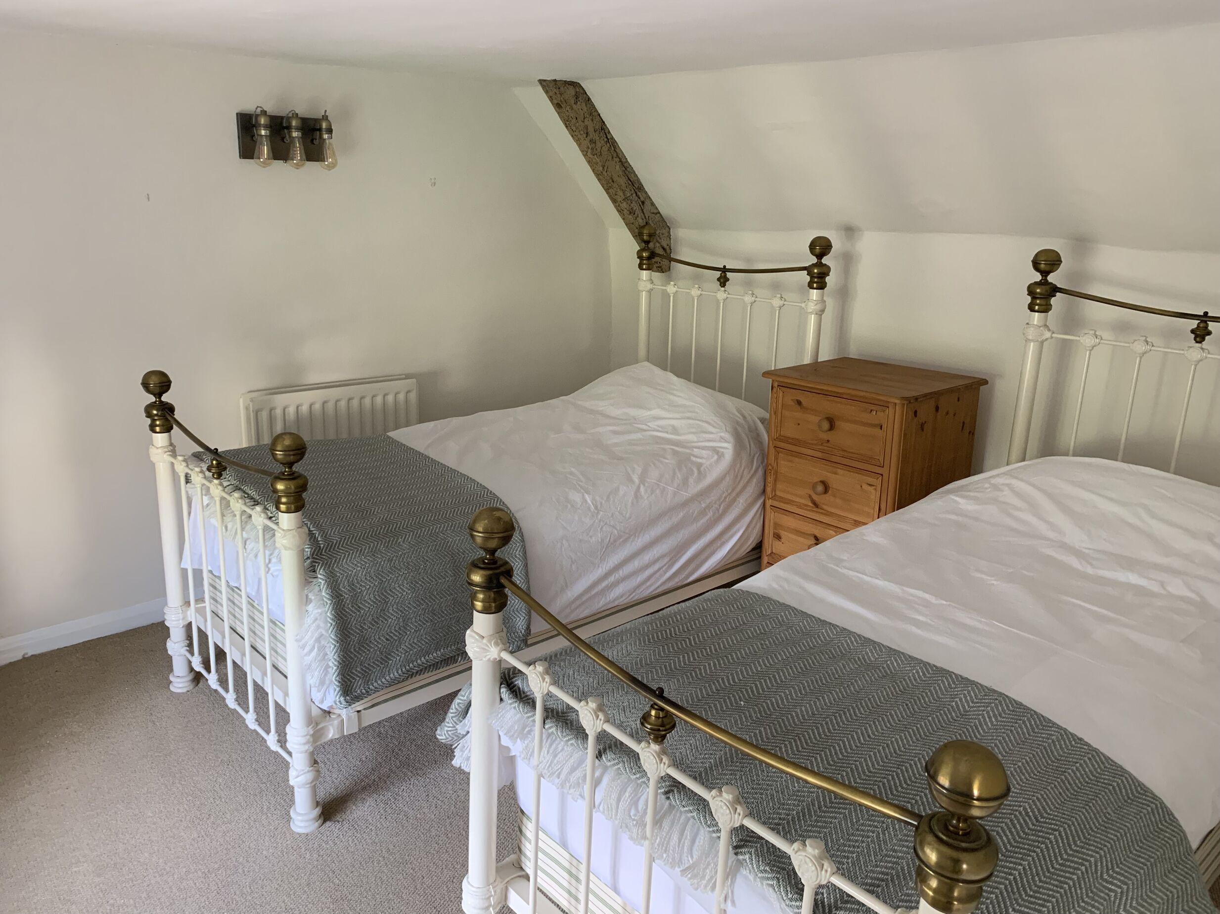 A bedroom with two single beds, a wooden nightstand, a radiator, and a small shelf with bottles.