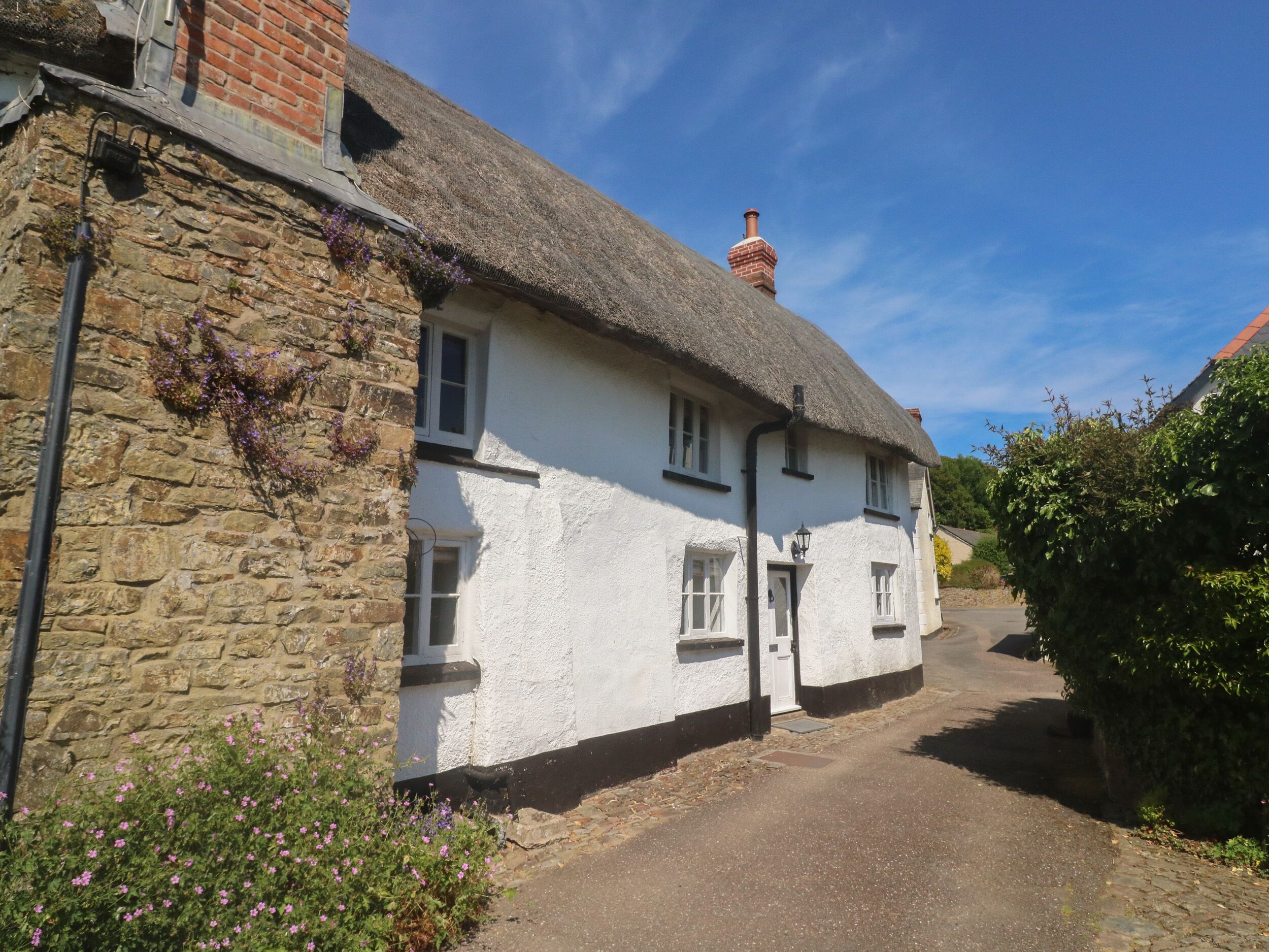 A traditional white building with a thatched roof, stone walls, and a narrow street.