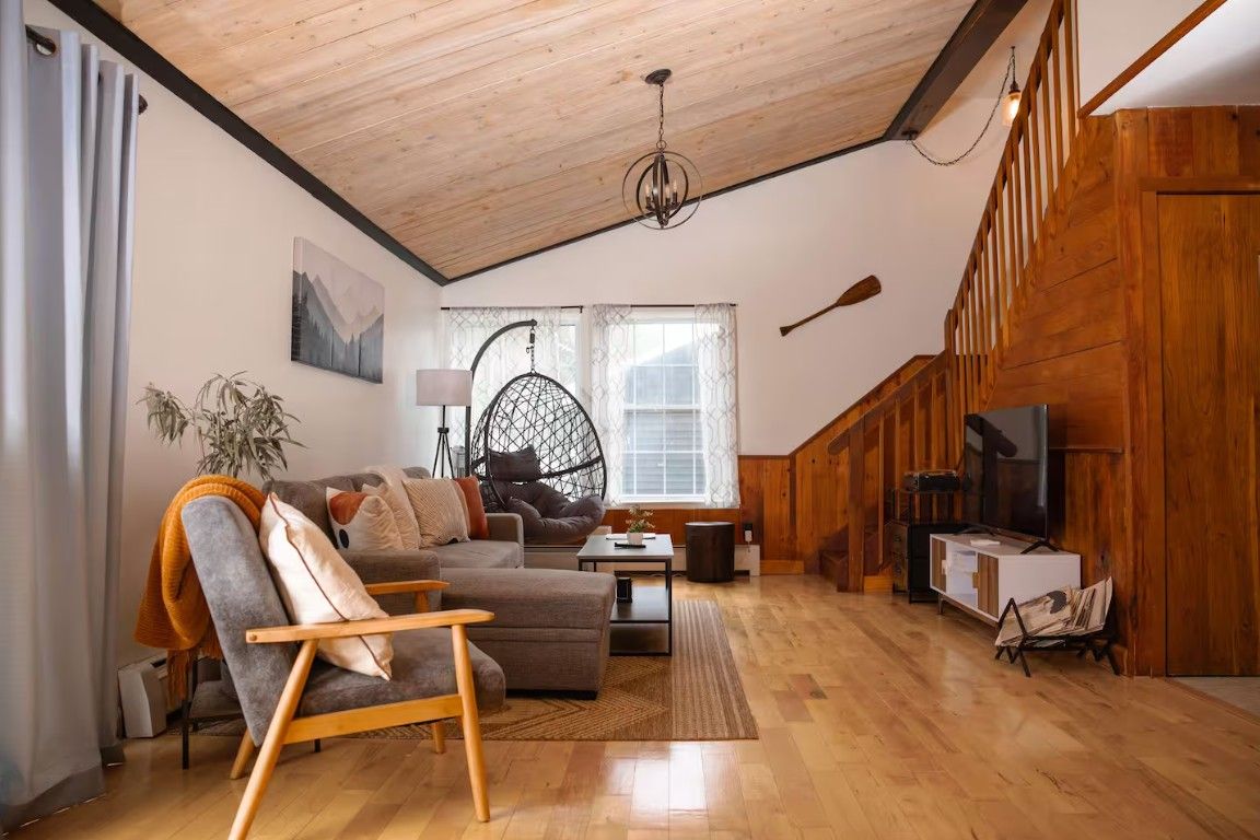 A cozy living room with a wooden ceiling, a sofa, a chair, and a television.