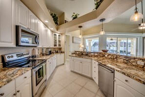 Une cuisine moderne avec des meubles blancs, des plans de travail en granit, des appareils électroménagers en acier inoxydable et des luminaires suspendus.