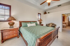 Un dormitorio con una cama de madera, dos mesitas de noche, un ventilador de techo y vistas al baño.