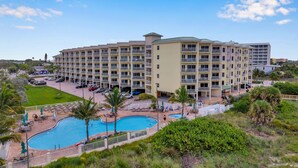A multi-story hotel with a swimming pool, outdoor seating, and a well-maintained lawn. - AMAZING BEACH VIEW/ FULLY REMODELED CONDO/ALL NEW FURNITURE/ HEATED POOL (Treasure Island)