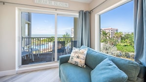 A balcony with a view of a pool and buildings, a sofa with a star-patterned pillow, and a sign reading "TREASURE ISLAND". - AMAZING BEACH VIEW/ FULLY REMODELED CONDO/ALL NEW FURNITURE/ HEATED POOL (Treasure Island)