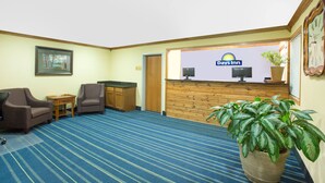 A reception area with a Days Inn sign, a reception desk, two armchairs, a small table, a potted plant, and a wooden wall panel. - Meridian Inn (Meridian)