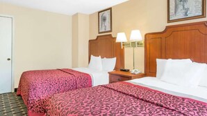 A hotel room with two beds, each with a pink patterned bedspread, wooden headboards, and bedside lamps. - Meridian Inn (Meridian)