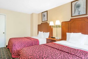 Habitación de hotel con dos camas, cada una con una colcha estampada de color rosa, cabeceros de madera y lámparas de noche.