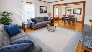 Un salon comprenant un canapé, une table basse, un coin repas et une grande fenêtre avec des rideaux.