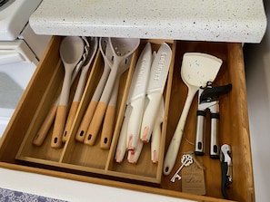 A drawer with various kitchen utensils including spoons, spatulas, and a bottle opener.