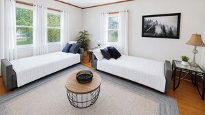 Une pièce avec deux lits, une table basse ronde, une plante en pot et un tableau encadré au mur.