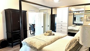 A four-poster bed with a white bedspread and multiple pillows, a dark wooden wardrobe, and a full-length mirror.