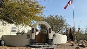 A building with an arched entrance, a flagpole with an American flag, and a desert landscape with rocks and sparse vegetation.