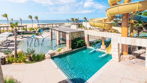 A pool area with a water slide, lounge chairs, and a view of the ocean.